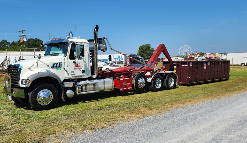 Roll-off dumpster truck delivering a large dumpster for waste removal.